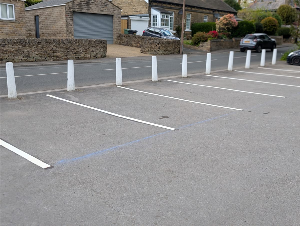 Roadside car park with freshly marked white thermoplastic parking bays alongside white bollards