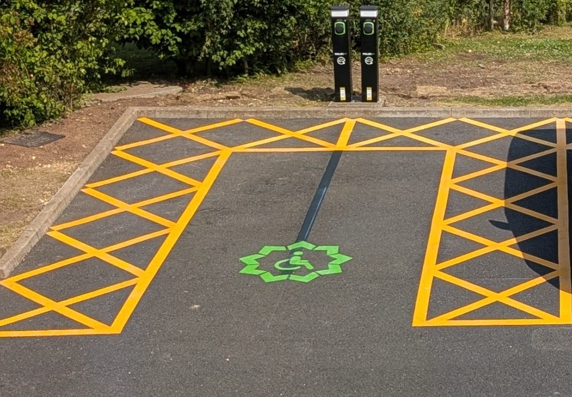 Disabled EV charging bay with yellow hatched access zones and green wheelchair symbol in thermoplastic