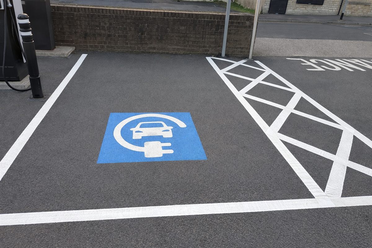 EV charging bay marked with a blue thermoplastic background, white car and plug symbol and white hatching